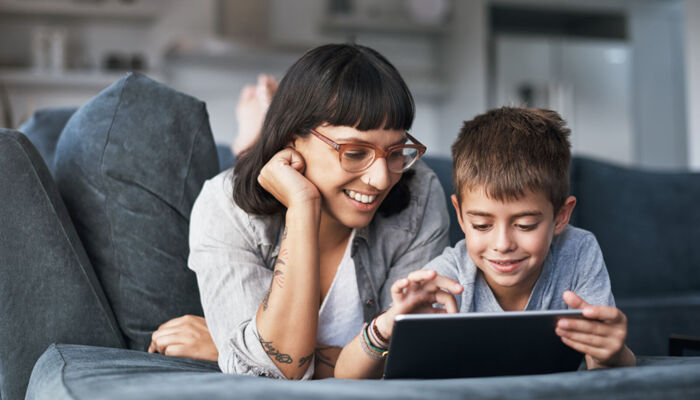 Mutter und kleiner Sohn, die zu Hause auf dem Sofa gemeinsam ein Tablet benutzen