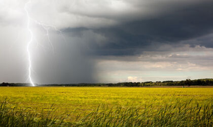 Ein heller Blitz schlägt in der Abenddämmerung auf einem Feld  ein